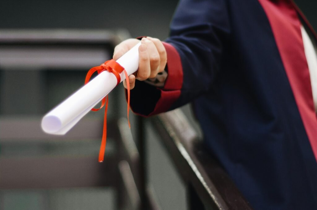 pexels-photo-2292837-2292837 A close-up image of a graduate holding a diploma tied with a red ribbon, symbolizing achievement and success.